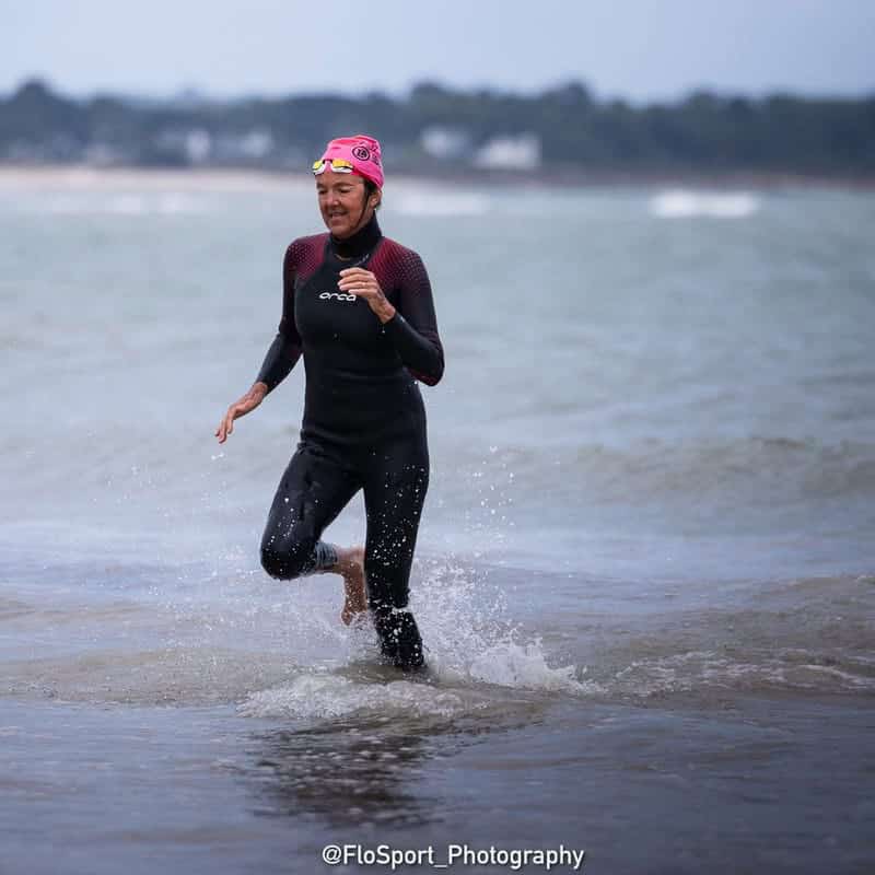 Photo d'une femme en combinaison de nage et bonnet qui courre au bord de l'eau