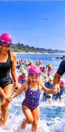 Une femme et une petite fille en combinaison de nage qui courent dans l'eau.